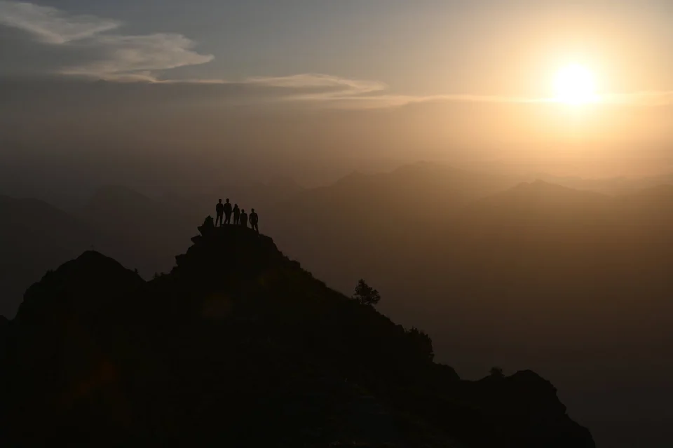 Silhouettes of the five musicians on a mountain ridge at sunset